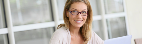 Woman wearing glasses in front of a computer, smiling at the camera